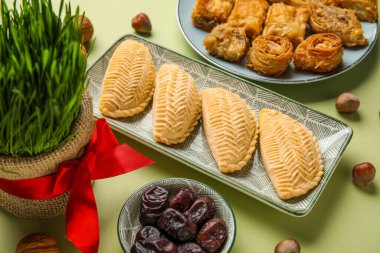 Plates with treats and grass on green background, closeup. Novruz Bayram celebration