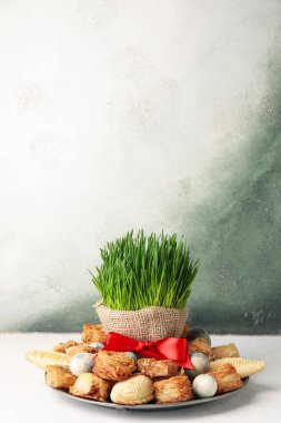 Plate with treats, eggs and grass on table near grunge wall. Novruz Bayram celebration