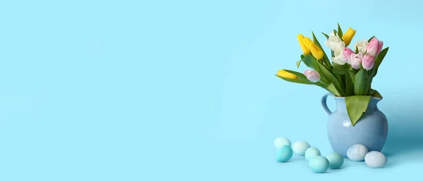 Vase with flowers and Easter eggs on light blue background with space for text