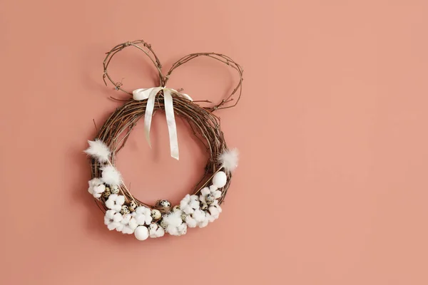 Easter wreath with cotton flowers and quail eggs on pink wall