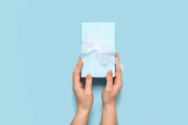 Female hands with gift box for Women's Day celebration on blue background