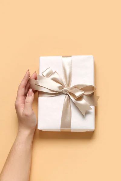 Female hand with gift box for Women's Day celebration on beige background