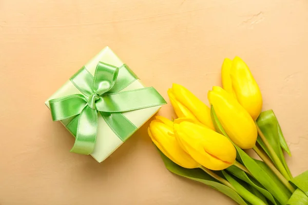 Gift box and beautiful tulip flowers on beige background. Hello spring
