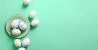 Plate and beautiful Easter eggs on turquoise background with space for text