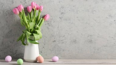 Vase with beautiful tulip flowers and painted Easter eggs on light background with space for text