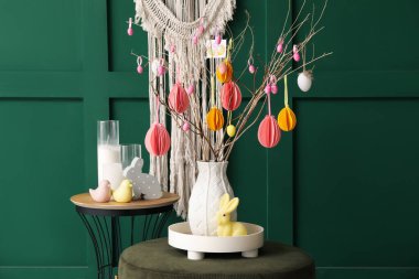 Table, pouf with tree branches and Easter eggs in vase near green wall