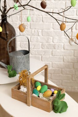 Vase with tree branches, Easter eggs, box and rabbits on tables in living room