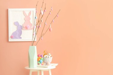 Vase with tree branches and Easter eggs on table in room