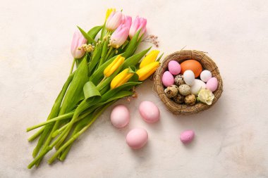 Bouquet of beautiful flowers and nest of Easter eggs on light background