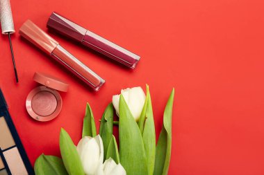 Composition with beautiful tulip flowers and decorative cosmetics on red background
