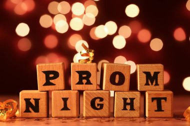 Wooden cubes with text PROM NIGHT on table against blurred lights