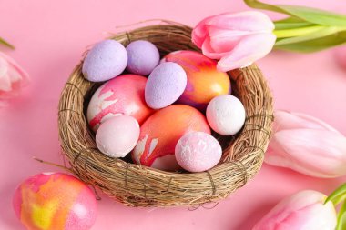 Nest with beautiful Easter eggs and tulip flowers on pink background