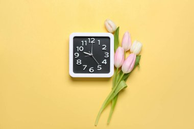 Alarm clock and beautiful tulip flowers on color background
