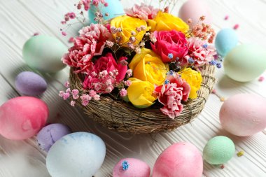 Composition with beautiful flowers and Easter eggs on light wooden background, closeup