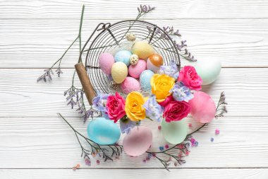 Composition with painted Easter eggs and beautiful flowers on light wooden background