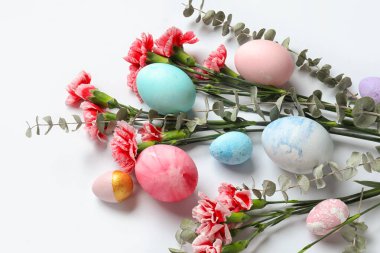 Composition with painted Easter eggs, carnation flowers and eucalyptus branches on white background, closeup