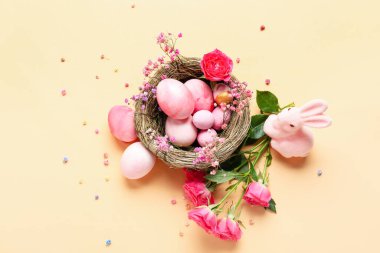 Composition with nest of painted Easter eggs, toy bunny and flowers on color background