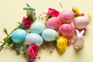 Composition with painted Easter eggs, flowers and ceramic bunnies on color background