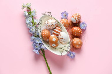 Composition with bowl of painted Easter eggs and beautiful flowers on pink background