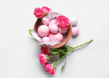 Composition with bowl of painted Easter eggs and rose flowers on white background
