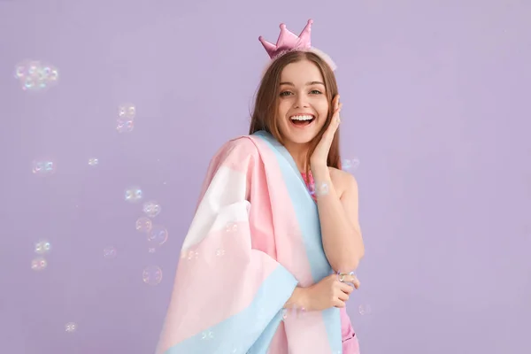 Young woman in crown with transgender flag and soap bubbles on lilac background