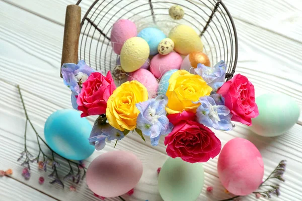 Composition with painted Easter eggs and beautiful flowers on light wooden background, closeup