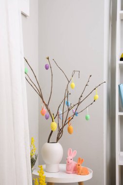 Vase with tree branches, Easter eggs and rabbits on table in living room