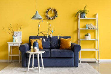 Vase with branches, painted eggs, Easter bunny and cake on end table in living room