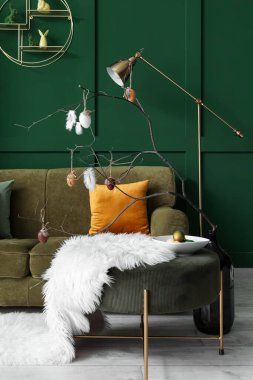 Vase with branches and painted Easter eggs on table in living room
