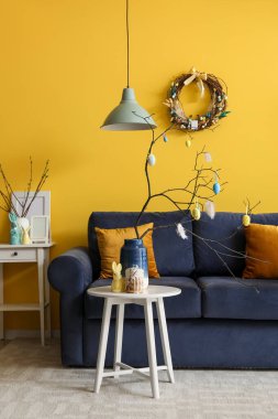 Vase with branches, painted eggs, Easter bunny and cake on end table in living room