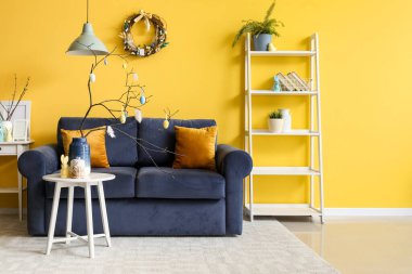 Vase with branches, painted eggs, Easter bunny and cake on end table in living room