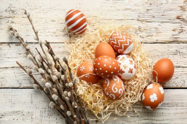 Nest with beautiful Easter eggs and willow branches on light wooden background