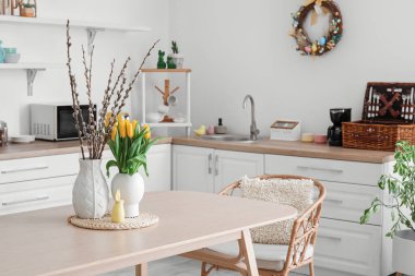 Vases with tulips, willow branches and Easter rabbit on dining table in kitchen