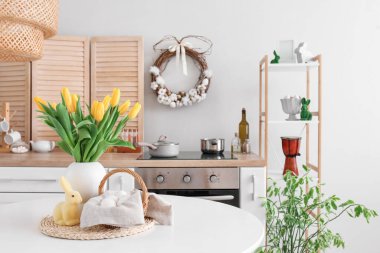 Vase with tulips, basket of Easter eggs and rabbit on dining table in kitchen