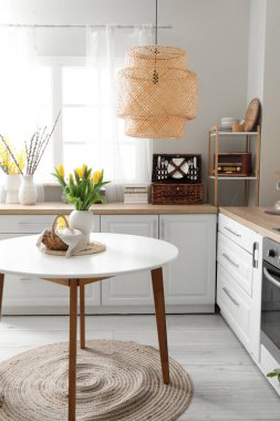 Vase with tulips, basket of Easter eggs and rabbit on dining table in kitchen