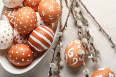 Bowl of painted Easter eggs and willow branches on light background, closeup