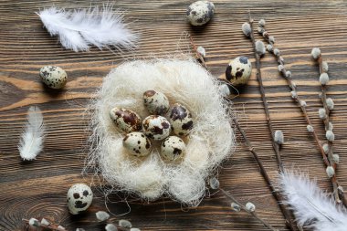 Composition with nest of Easter eggs, feathers and willow branches on wooden background