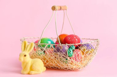 Basket with Easter eggs, candies and bunny on pink background