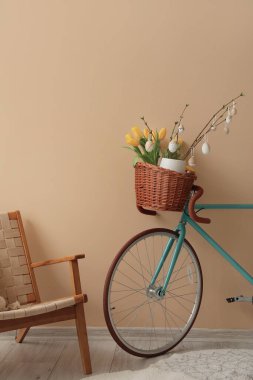 Bicycle with tree branches, Easter eggs and tulips near beige wall