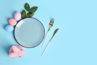 Table serving with Easter eggs, cutlery and bunny on blue background