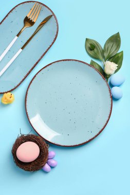 Table serving with Easter eggs, cutlery and eustoma flower on blue background