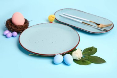 Table serving with Easter eggs, cutlery and eustoma flower on blue background