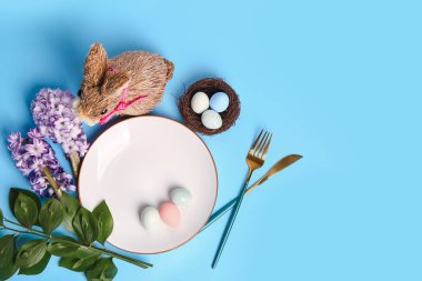 Table serving with Easter eggs, bunny, cutlery and hyacinth flowers on blue background