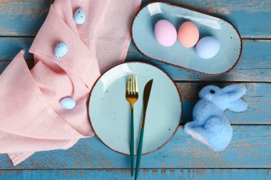 Table serving with Easter eggs and bunny on blue wooden background
