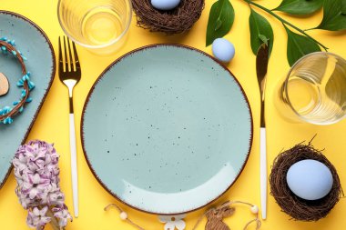 Table setting with Easter eggs, cutlery and hyacinth flowers on yellow background