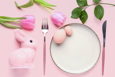 Table setting with Easter eggs, tulip flowers, cutlery and bunny on pink background