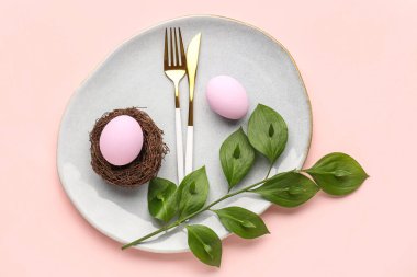 Table setting with Easter eggs, cutlery and plant branch on pink background