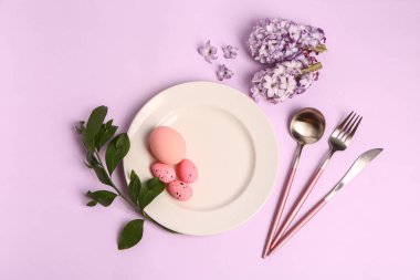 Table serving with Easter eggs, hyacinth flowers and green plant branch on lilac background
