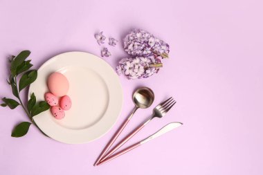 Table serving with Easter eggs, hyacinth flowers and plant branch on lilac background