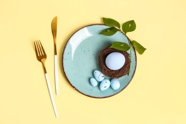 Table serving with Easter eggs and green plant branch on yellow background